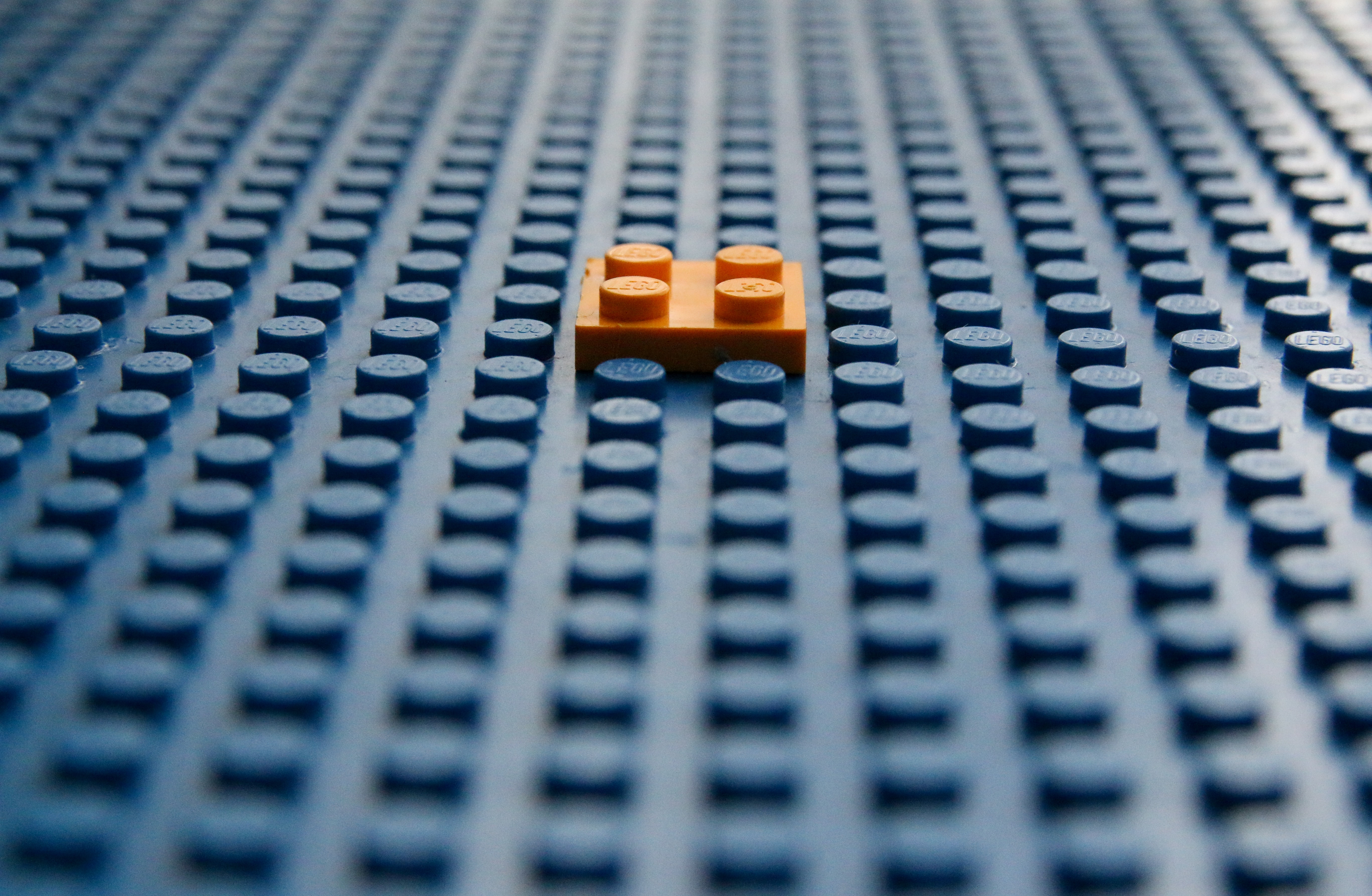 one orange lego piece stuck to a blue lego board.